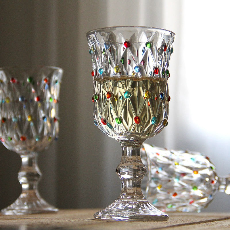 Decorative glass goblets with multicolored dots on a wooden surface.