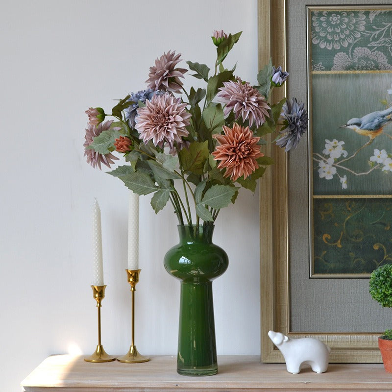 Green vase with flowers on a shelf next to candles and a framed picture