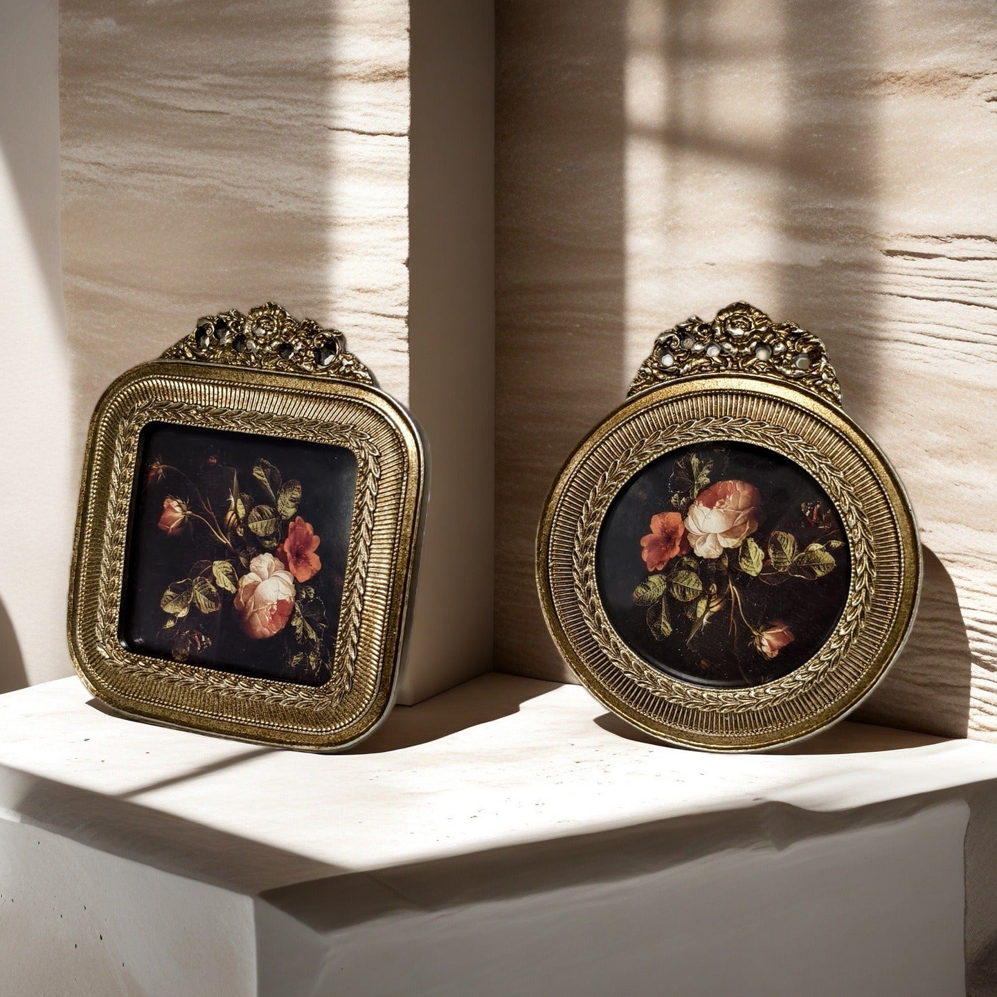 Two ornate gold frames with floral artwork on a textured wall.