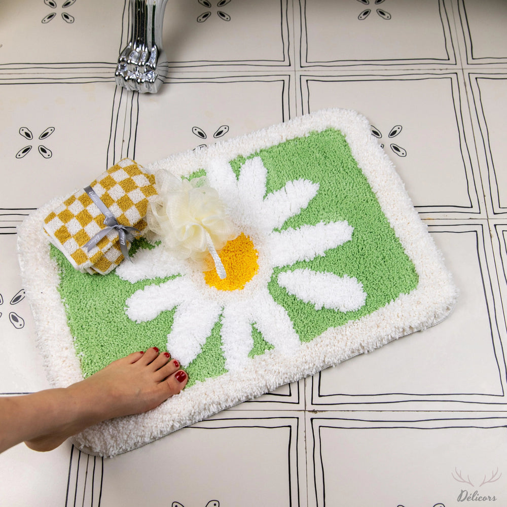 Green bath mat with white flower design on a tiled bathroom floor.