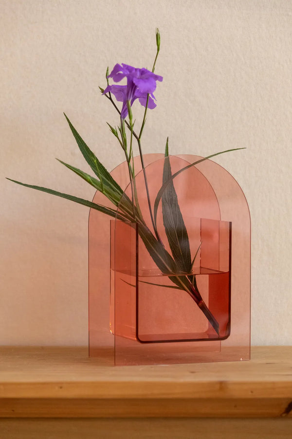 A translucent peach-pink acrylic arch-shaped vase with a rectangular water-filled center