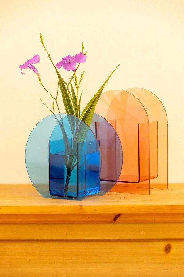A translucent acrylic vase with a rounded rectangular shape in blue, holding green stems