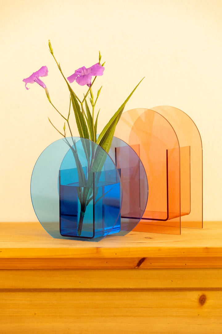 A translucent acrylic vase with a rounded rectangular shape in blue, holding green stems